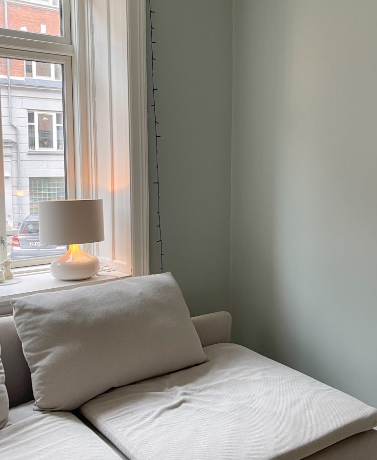 Efterbillede lys sofa i grøn stue med puder og lampe i vindue