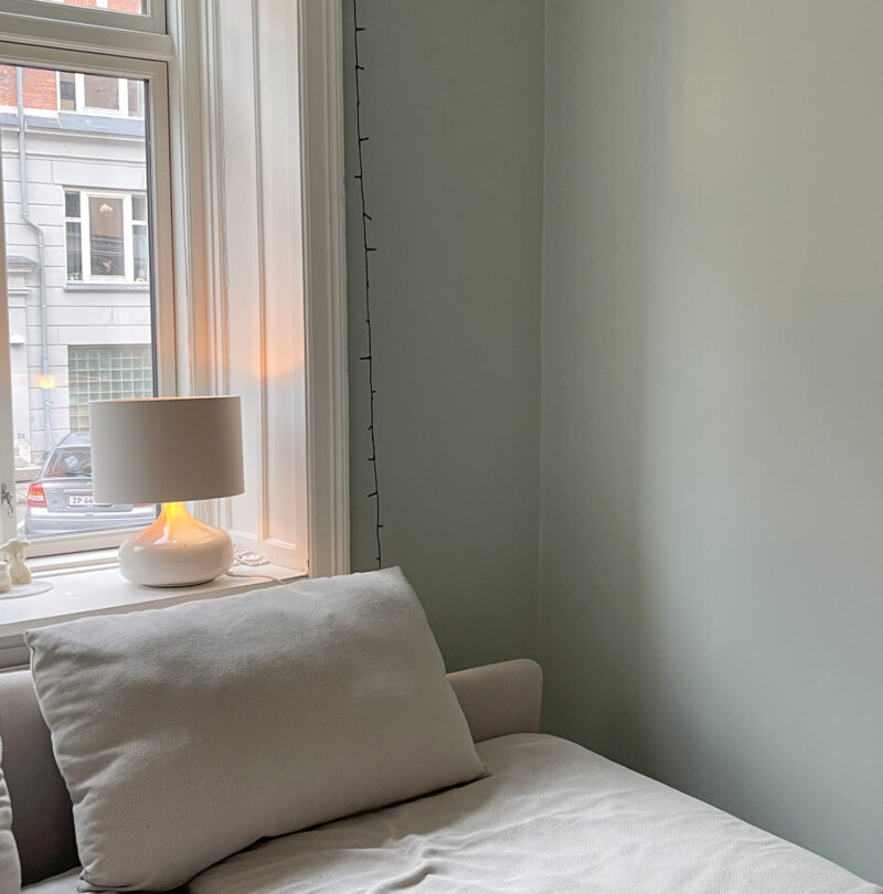 Efterbillede lys sofa i grøn stue med puder og lampe i vindue