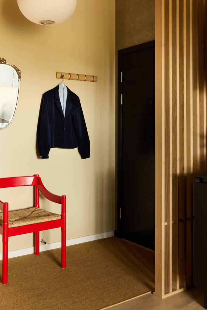 Entre indrettet i bløde nuancer, skillevæg i træ og en rød stol som blikfang